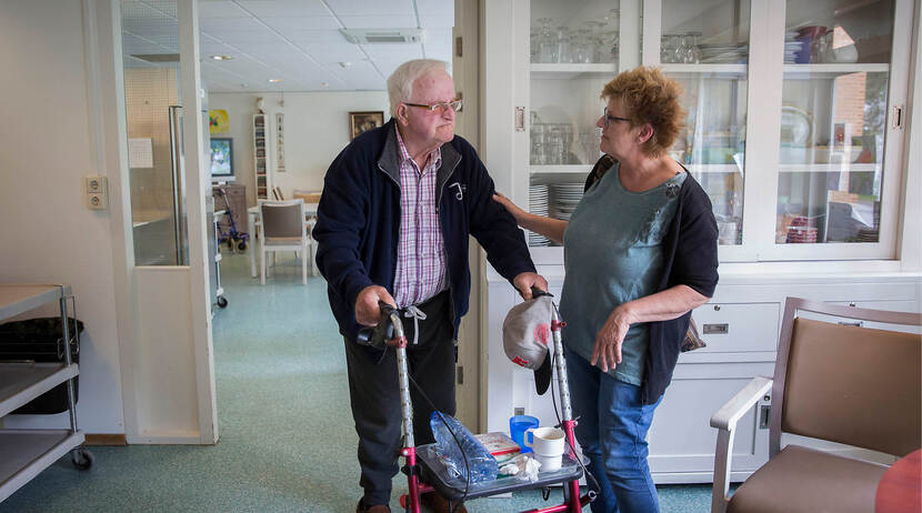 KIK-V Oudere meneer met rollator en zorgmedewerkster in een verpleeghuis
